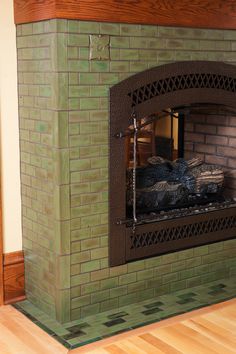 a brick fireplace in a living room with wood flooring and green tiles on the wall