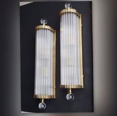 two wall lights mounted on the side of a black and gold wall with clear glass shades