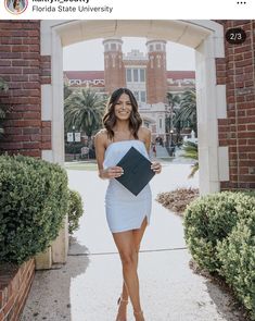 a woman in a white dress is holding a black book and smiling at the camera