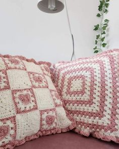 two pink and white crocheted pillows sitting on a couch next to a lamp