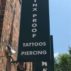 there is a sign that says tattoo piercing next to a brick building with trees in the background