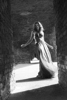 a woman in a long dress is walking through an alley way with brick walls and arches