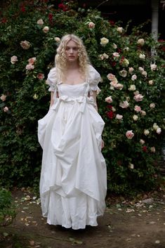 a woman wearing a white dress standing in front of flowers