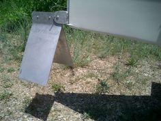 a metal sign sitting on the side of a road next to some grass and trees