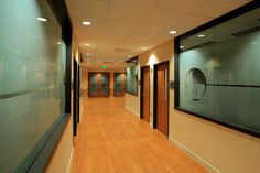 an empty hallway with wooden floors and glass doors on the walls, leading to two elevators