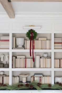 bookshelves with wreath and pine cones on them in front of white painted walls