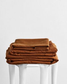 a stack of brown blankets sitting on top of a white stool next to a wall