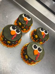 four cupcakes decorated with green frosting and orange icing are sitting on a silver surface