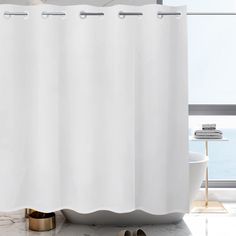 a white shower curtain in a bathroom next to a bathtub with a pair of slippers on the floor