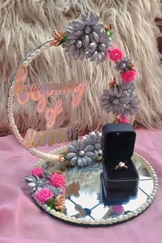 a ring is sitting on top of a glass plate with flowers around it and a box in the middle