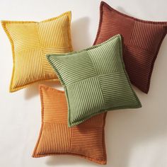 three decorative pillows in different colors on a white surface, one is orange and the other is green