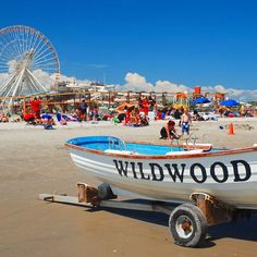 a white boat sitting on top of a sandy beach next to a carnival ferris wheel