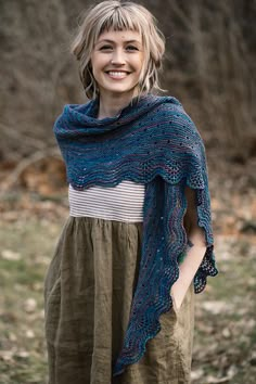 a woman wearing a blue knitted shawl standing in a field with her hands on her hips