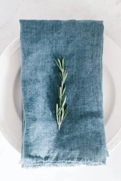 a napkin with a sprig of rosemary on it sitting on top of a white plate