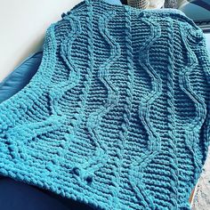 a blue crocheted blanket sitting on top of a bed next to a vase