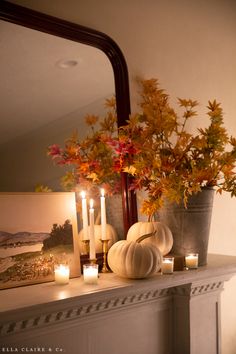 a mantle with candles, pumpkins and flowers on it in front of a mirror