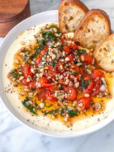 a white bowl filled with bread and vegetables on top of a marble counter next to a cup of coffee