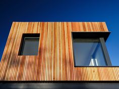 the side of a building with two windows and wood slats on it's sides