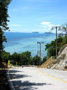 an empty road with power lines and telephone poles on both sides, overlooking the ocean