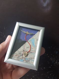 a hand holding a small white frame with a map in it and a bird on top