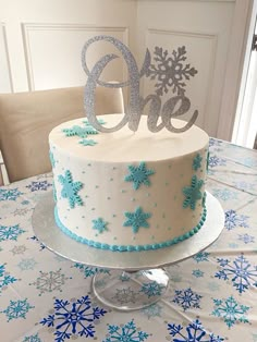 a white cake with blue frosting and snowflakes on the top is sitting on a table