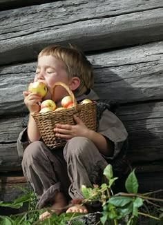 a young boy sitting on the ground holding an apple basket