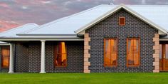 a brick house with three windows and white pillars on the front lawn at sunset or dawn