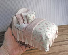 a hand is holding a small bed with pink flowers on it and ruffled edges