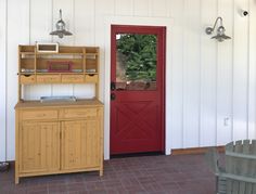 a red door in front of a white wall with a wooden hutch next to it