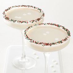 two martini glasses with christmas sprinkles on them sitting on a white tray