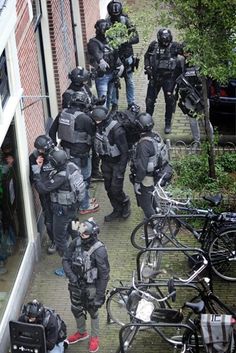 several police officers in full riot gear and helmets are standing near bicycles on the sidewalk