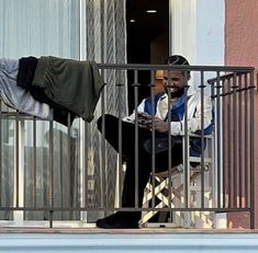 a man sitting on top of a balcony next to a metal railing holding a cell phone