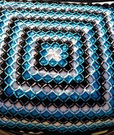 a blue and black crocheted blanket on top of a metal table with an object in the middle