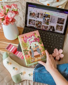 a person sitting on a bed with a laptop and book in front of them, surrounded by flowers