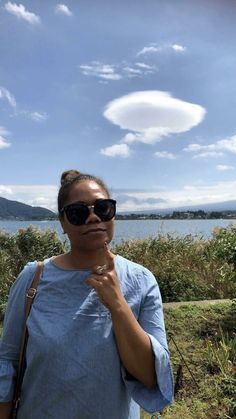 a woman wearing sunglasses is standing by the water and holding her finger up to her mouth