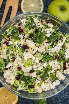 a bowl filled with broccoli, cauliflower and raisins next to an apple