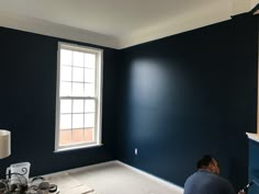 a man is painting the walls of a room with dark blue paint and white trim