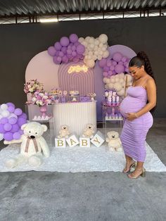 a pregnant woman standing in front of a table with balloons and teddy bears on it