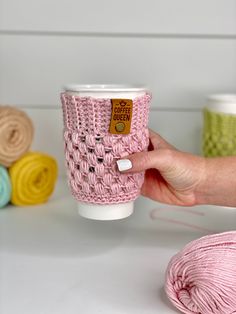 a hand holding a pink knitted coffee cup