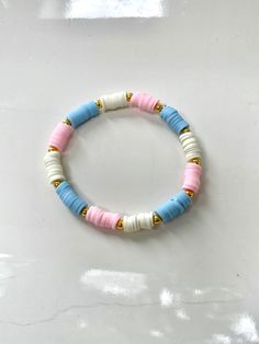 a white and blue beaded bracelet with gold accents on a white surface, the beads are made out of plastic