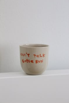 a white cup with red writing on it sitting on top of a shelf next to a vase