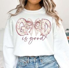 a woman wearing a white sweatshirt with the words god is good on it and a pink bow