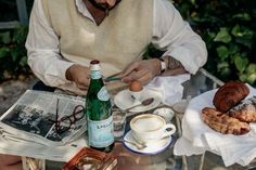 a man sitting at an outdoor table with pastries, coffee and croissants