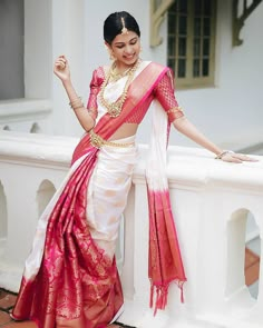 a woman in a white and pink sari leaning on a wall with her hand on her hip