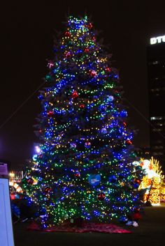 a large christmas tree is lit up with multicolored lights in the city at night