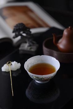 a bowl of tea sits on a table next to an open book