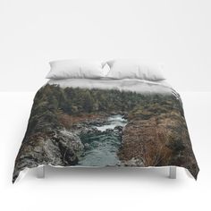 a bed with a river and trees in the background on top of it, next to a white wall