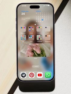 an iphone with the home screen open and flowers in front of it on a table