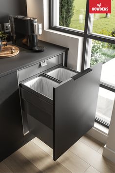 an open dishwasher sitting on top of a counter next to a window