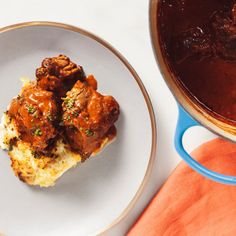 a white plate topped with meat and gravy next to a pot of stew